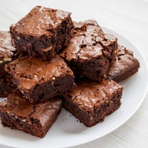 Homemade chocolate brownies on a white plate on a white wooden background, side view. Copy space.