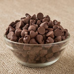A glass bowl of chocolate chips on a textured tablecloth.