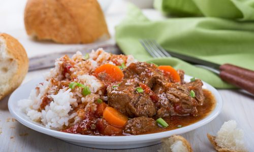 Homemade beef and vegetable casserole served with rice on white plate, comfort food for a cold day