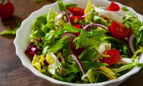 various fresh mix salad leaves with tomato in bowl on wooden background